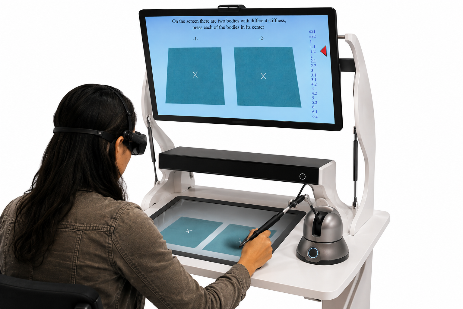 Haptic-based virtual reality sensory testing system: user wearing 3D glasses and using a haptic stylus on a touch-sensitive tablet to press the center of two virtual bodies of different stiffness shown on the main screen
